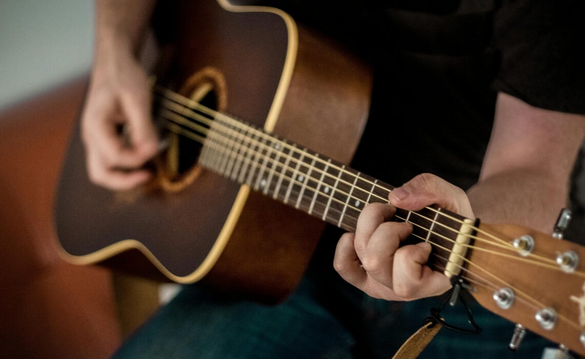 Person playing an acoustic guitar, focusing on chord transitions and finger placement.