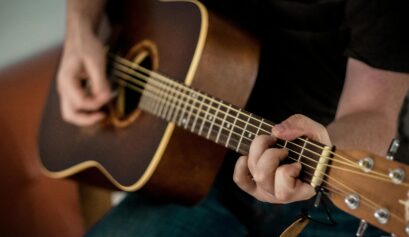 Person playing an acoustic guitar, focusing on chord transitions and finger placement.