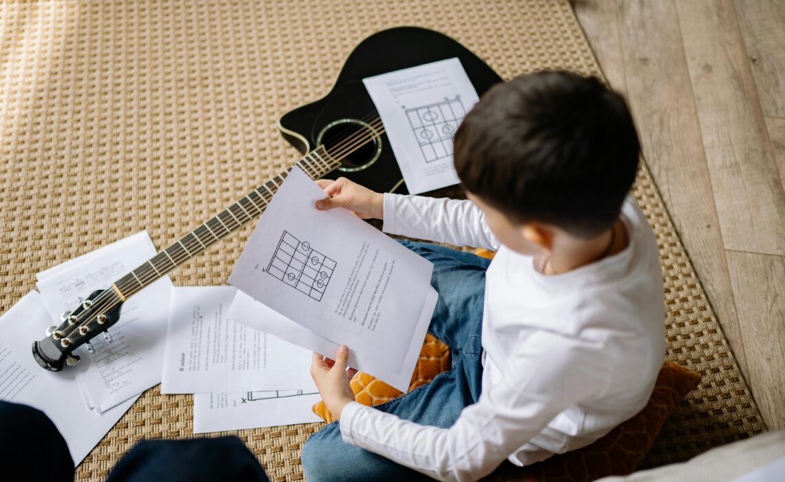 kid learning to read musical notes on an acoustic guitar, practicing sheet music for easy guitar lessons.