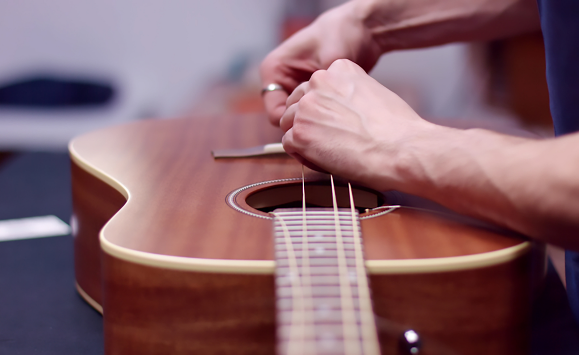 A person changing acoustic guitar strings, carefully replacing old strings with new ones while tuning the guitar for optimal sound quality.