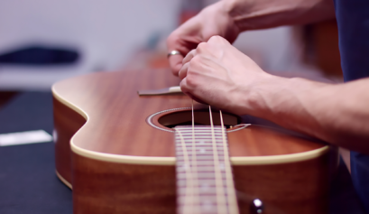 A person changing acoustic guitar strings, carefully replacing old strings with new ones while tuning the guitar for optimal sound quality.